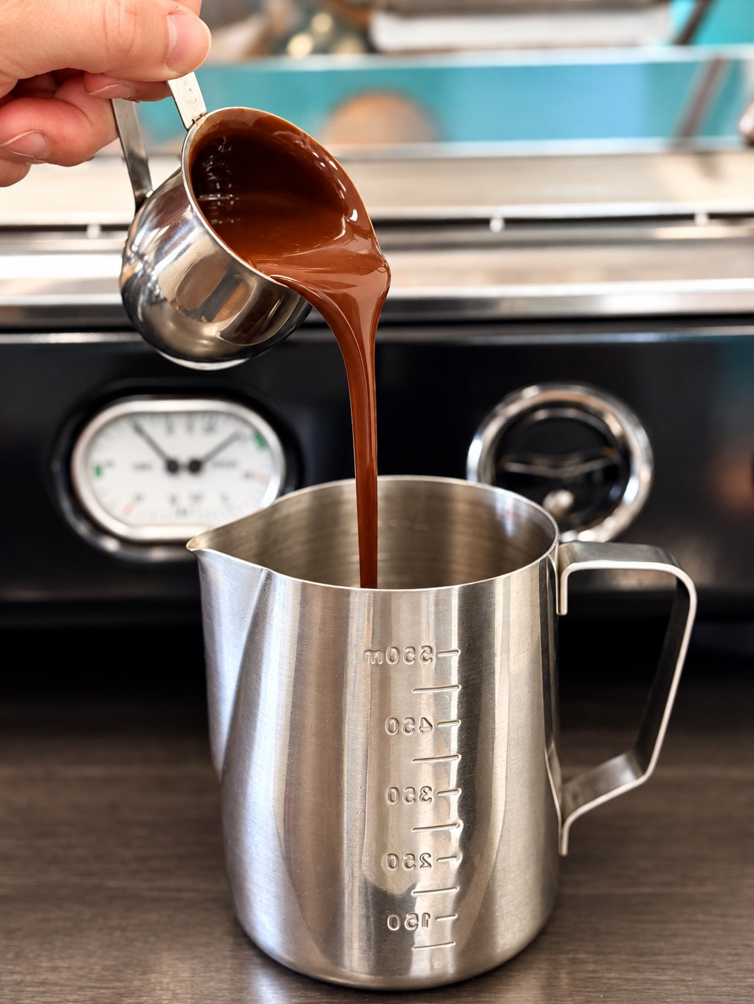 Chocolate sauce poured into a stainless-steel pitcher