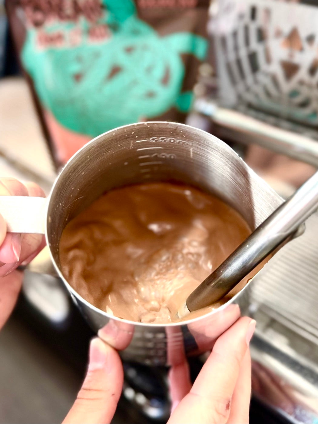 Chocolate being steamed in a stainless-steel pitcher